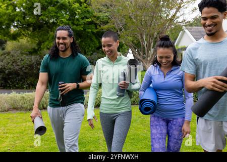 Multirassische Freunde laufen im Park mit Yogamatten, lächeln und genießen Outdoor-Übungen Stockfoto