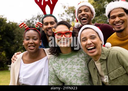 Festliche Hüte tragen, multirassische Freunde feiern Weihnachten im Freien, lachen fröhlich zusammen Stockfoto