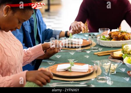 Weihnachtszeit, junge multirassische Freunde, die Hände an festlichen Tisch halten, zu Hause Stockfoto