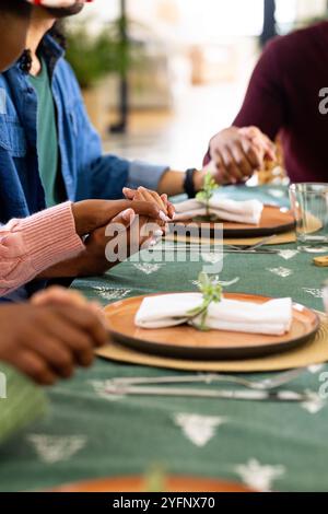 Weihnachtszeit, multirassische Freunde, die Hände um den festlichen Tisch halten, zu Hause Stockfoto