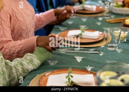 Weihnachtszeit, multirassische Freunde halten Hände an festlichen Esstisch, zu Hause Stockfoto