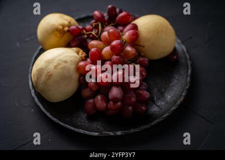 Haufen von roten Trauben und gelben Birnen auf einer schwarzen Glimmerplatte auf dunklem Hintergrund. Hochwertige Fotos Stockfoto