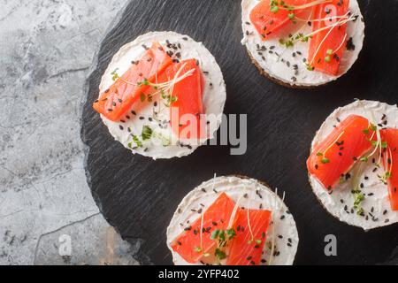 Smorrebrod traditionelles dänisches Sandwich mit schwarzem Roggenbrot, Lachs, Frischkäse, Sesam und Mikrogemüse für gesundes Frühstück Nahaufnahme auf Schieferbrot pla Stockfoto