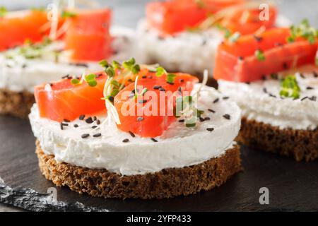 Gesundes Roggenbrot-Sandwich mit rotem Fisch, Frischkäse, Sesam und Microgreens Nahaufnahme auf Schieferplatte auf dem Tisch. Horizontal Stockfoto