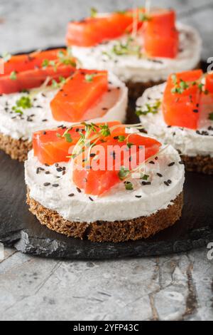 Canape Sandwich mit rotem Fisch, Frischkäse, Sesam und Mikrogrün in Nahaufnahme auf Schieferplatte auf dem Tisch. Vertikal Stockfoto