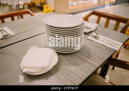 Dutzende von Tellern und Servietten sind ordentlich auf einem Tisch in einem Hotelrestaurant angeordnet Stockfoto