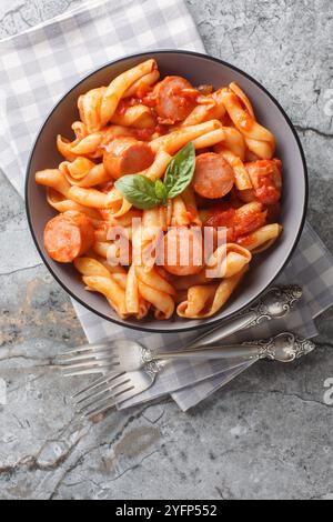 Treccione Nudeln mit Tomaten, Zwiebeln, Wurst und Gewürzen in einer Schüssel auf dem Tisch. Vertikale Draufsicht von oben Stockfoto
