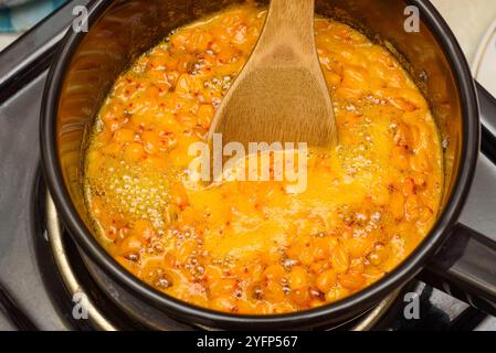 Kochende Sanddornbeeren mit Zucker in einem Topf mit einem Holzlöffel rühren. Hausmannskost. Stockfoto