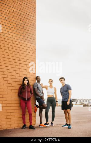 Verschiedene Gruppen junger Erwachsener posieren selbstbewusst in trendiger Sportkleidung vor einer urbanen Backsteinmauer. Stockfoto