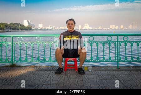 Ein vietnamesischer Mann mittleren Alters in Fahrradkleidung ruht an einem Sonntagmorgen neben dem Westsee in Hanoi, Vietnam. Stockfoto