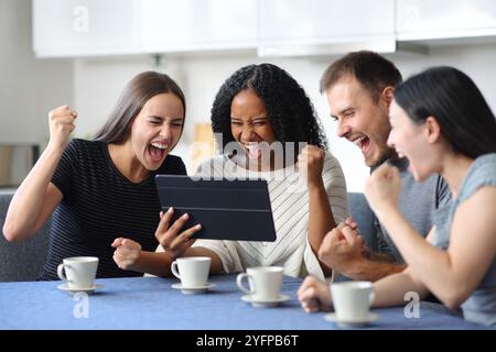 Vier begeisterte interrassische Freunde sehen sich Medien auf einem Tablet in der Küche zu Hause an Stockfoto