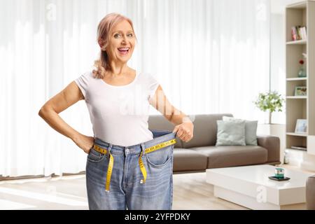 Glückliche Frau mittleren Alters, die zu Hause eine Jeans anprobiert, Gewichtsreduktion Konzept Stockfoto