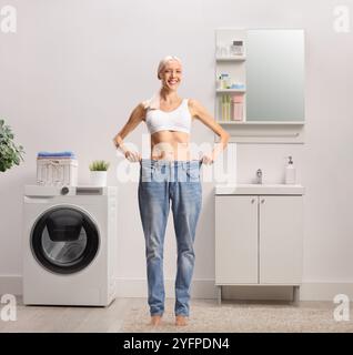 Junge Frau im Badezimmer, die Jeans anprobiert, Gewichtsreduktion-Konzept Stockfoto