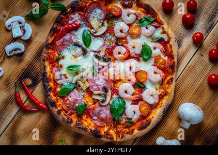 Pizza mit zwei Toppings, eine halbe Paperoni mit Pilzen, die anderen Tomaten und Garnelen mit Käse. Pizza auf einem Holztisch mit Zutaten Stockfoto