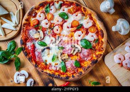 Pizza mit zwei Toppings, eine halbe Paperoni mit Pilzen, die anderen Tomaten und Garnelen mit Käse. Pizza auf einem Holztisch mit Zutaten Stockfoto