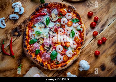 Pizza mit zwei Toppings, eine halbe Paperoni mit Pilzen, die anderen Tomaten und Garnelen mit Käse. Pizza auf einem Holztisch mit Zutaten Stockfoto