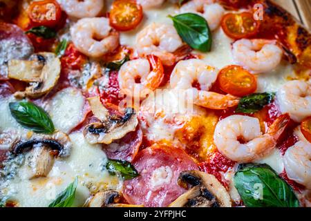 Pizza mit zwei Arten von Belägen: Eine Hälfte Peperoni mit Pilzen, die andere mit Tomaten und Garnelen mit Käse. Hintergrund mit Pizza-Textur. Stockfoto