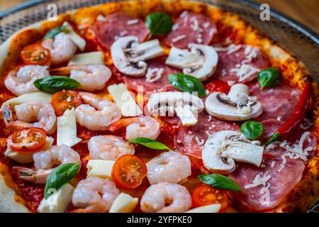 Pizza mit zwei Arten von Belägen: Eine Hälfte Peperoni mit Pilzen, die andere mit Tomaten und Garnelen mit Käse. Hintergrund mit Pizza-Textur. Stockfoto