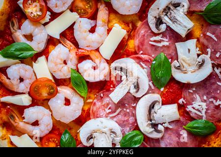 Pizza mit zwei Arten von Belägen: Eine Hälfte Peperoni mit Pilzen, die andere mit Tomaten und Garnelen mit Käse. Hintergrund mit Pizza-Textur. Stockfoto