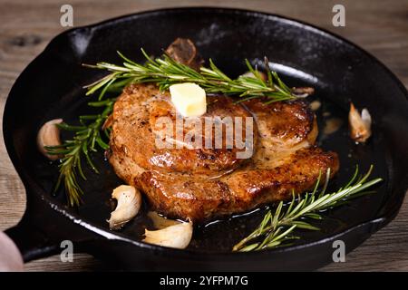 Schweinekotelett auf dem Knochen in einem Stück Butter mit Knoblauch und Rosmarin in einer Pfanne Stockfoto