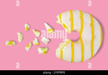 Fehlendes Stück weiße Schokolade und gelbe Streifen Donut mit Krümeln auf rosa Hintergrund. Stockfoto