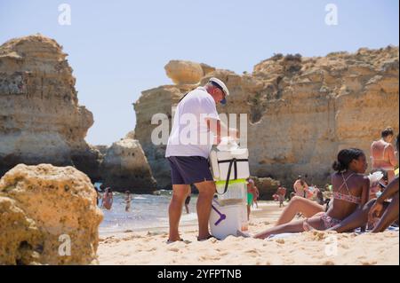 Ein freundlicher Verkäufer verkauft eine traditionelle Bola de Berlim an einen Strandgänger im Praia de São Rafael, eingerahmt von den Klippen der Algarve Stockfoto