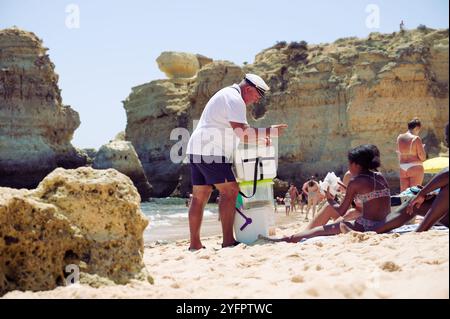 Ein freundlicher Verkäufer verkauft eine traditionelle Bola de Berlim an einen Strandgänger im Praia de São Rafael, eingerahmt von den Klippen der Algarve Stockfoto