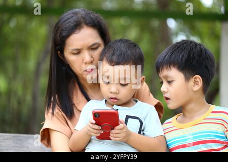 Eine Mutter und ihre beiden Kinder nutzen ein Smartphone in einer natürlichen Umgebung und zeigen Momente der Neugier und Verbindung in einem entspannten Outdoor-atmos Stockfoto