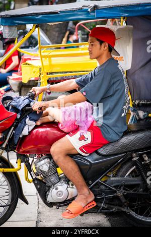 Ein junger philippinischer Mann sitzt auf seinem Trike im Verkehr, und seine kleine Tochter saß auf seinem Schoß in Manila City, den Philippinen. Stockfoto