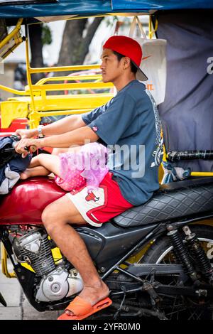 Ein junger philippinischer Mann sitzt auf seinem Trike im Verkehr, und seine kleine Tochter saß auf seinem Schoß in Manila City, den Philippinen. Stockfoto