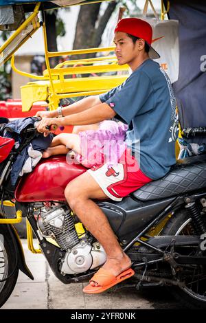 Ein junger philippinischer Mann sitzt auf seinem Trike im Verkehr, und seine kleine Tochter saß auf seinem Schoß in Manila City, den Philippinen. Stockfoto