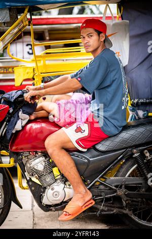 Ein junger philippinischer Mann sitzt auf seinem Trike im Verkehr, und seine kleine Tochter saß auf seinem Schoß in Manila City, den Philippinen. Stockfoto