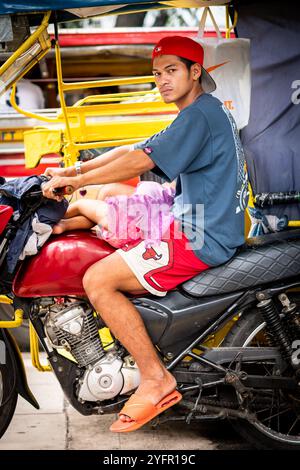 Ein junger philippinischer Mann sitzt auf seinem Trike im Verkehr, und seine kleine Tochter saß auf seinem Schoß in Manila City, den Philippinen. Stockfoto