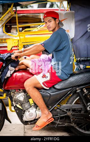 Ein junger philippinischer Mann sitzt auf seinem Trike im Verkehr, und seine kleine Tochter saß auf seinem Schoß in Manila City, den Philippinen. Stockfoto