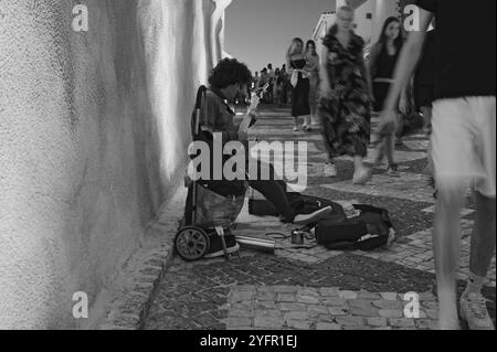 Straßenmusiker spielt Gitarre auf einem belebten Kopfsteinpflaster in Albufeira Stockfoto