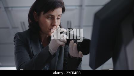 Büroraub oder Mordfall: Nahaufnahme einer Kriminalistin, die mit einer professionellen Kamera Beweisaufnahmen am Tatort macht. Ein männlicher Detective kommt, spricht mit einem Kollegen. Das Untersuchungsteam arbeitet. Stockfoto