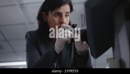 Büroraub oder Mordfall: Nahaufnahme einer Kriminalistin, die mit einer professionellen Kamera Beweisaufnahmen am Tatort macht. Ein männlicher Detective kommt, spricht mit einem Kollegen. Das Untersuchungsteam arbeitet. Stockfoto