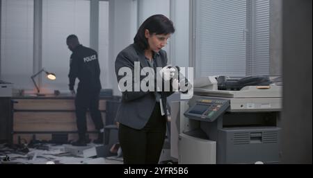 Büroraub oder Mordfall: Das Ermittlungsteam arbeitet am Tatort. Eine Kriminalistin fotografiert Beweise mit der Kamera. Der afroamerikanische Polizist sucht Fingerabdrücke im Hintergrund. Stockfoto