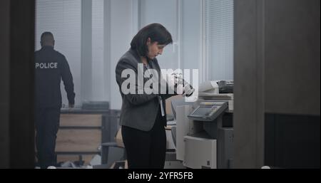 Büroraub oder Mordfall: Das Ermittlungsteam arbeitet am Tatort. Eine Kriminalistin macht Fotos von Beweisen. Afroamerikanischer Polizist sucht nach Fingerabdrücken, Detective kommt in den Raum. Stockfoto