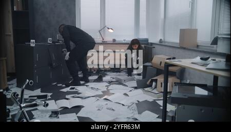 Multiethnisches Ermittlungsteam arbeitet am Tatort: Kriminalistin fotografiert Beweise, afroamerikanische Kriminalpolizei sucht nach Fingerabdrücken. Banküberfall oder Mordfall. Stockfoto