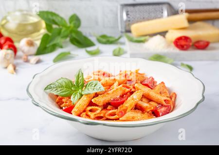 Klassische italienische Pasta Penne alla arrabiata mit Basilikum und frisch geriebenem Parmesankäse auf dunklem Tisch. Penne mit Chilisauce arrabbiata. Stockfoto