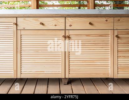 Holzschränke der Außenküche mit Lamellen, Schubladen, Holzgriffen und Sperrholzplatte stehen auf einer Holzterrasse Stockfoto