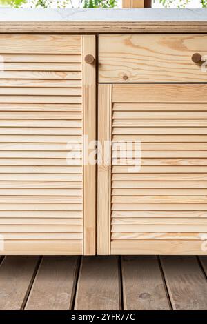 Holzschränke der Außenküche mit Lamellentüren, Schubladen, Holzgriffen und Sperrholzplatte stehen auf einer Holzterrasse aus nächster Nähe Stockfoto