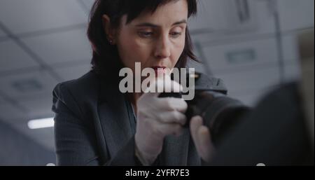 Büroraub oder Mordfall: Nahaufnahme einer Rechtswissenschaftlerin oder Kriminalistin, die mit einer professionellen Kamera Beweisaufnahmen am Tatort macht. Das Untersuchungsteam arbeitet. Kriminologisches Konzept Stockfoto
