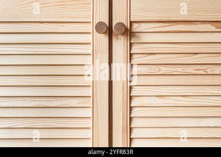 Holztüren mit Lamellen und Holzgriff in Nahaufnahme. Die Türen der Außenküche sind aus hellem Kiefernholz mit natürlichem Masermuster gefertigt Stockfoto