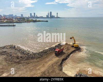 Bagger mit einem LKW mit Sand arbeitet an der Küste vor dem Hintergrund der Stadt Batumi, Blick von einer Drohne. Stockfoto