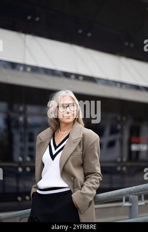 Ältere Geschäftsfrau steht selbstbewusst vor ihrem Büro in professioneller Kleidung an einem sonnigen Tag Stockfoto