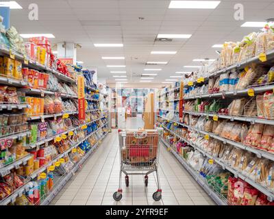 Cremona, Lombardei, Italien 27. Oktober 2024 Leerer Einkaufswagen steht im Supermarktgang zwischen Regalen voller verschiedener Produkte, was auf Begi hindeutet Stockfoto