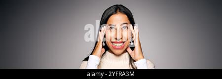 Eine fröhliche junge Frau lächelt breit, während sie ihr Gesicht berührt, und strahlt Freude und Wärme aus. Stockfoto