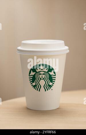 Eine Starbucks Kaffeetasse steht auf einem Holztisch und zeigt das kultige grün-weiße Logo der Marke. Stockfoto